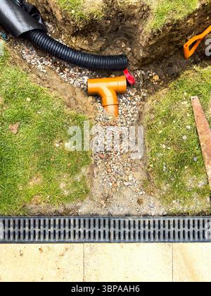 Rohrverlegung und Grabenaushub auf einem grasbewachsenen Rasen für die Installation von Drainage und Landschaftsgestaltung bei Neubauprojekten Stockfoto