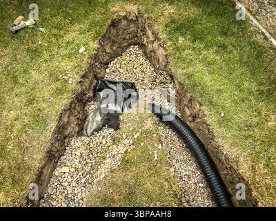 Rohrverlegung und Grabenaushub auf einem grasbewachsenen Rasen für die Installation von Drainage und Landschaftsgestaltung bei Neubauprojekten Stockfoto