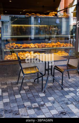 Dänisches Gebäck: Viele verschiedene süße Brötchen werden in der Bäckerei durch das Fenster von der Straße aus hergestellt. Stühle und Tisch stehen draußen in der Nähe der Bäckerei Stockfoto
