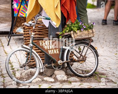 Vaxholm, Schweden - 4. Juni 2025: Ein Oldtimer-Fahrrad mit der Aufschrift „RENT BIKE HERE“ steht neben einem Korb mit bunten Decken Stockfoto