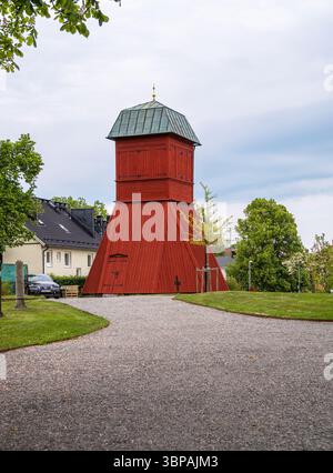 Vaxholm, Schweden - 4. Juni 2025: Ein markanter roter Holzturm mit grünem Dach, der vor einem bewölkten Himmel steht. Der Turm ist von üppigem Grün umgeben und Stockfoto