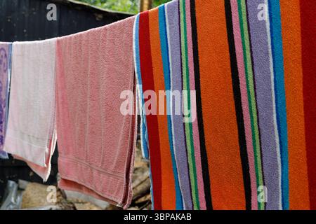 Farbenfrohe Handtücher hängen draußen in der Sonne, mit hellen Streifen und Texturen, perfekt für einen warmen Sommertag und Innenkomfort mit lebendigem Ambiente Stockfoto