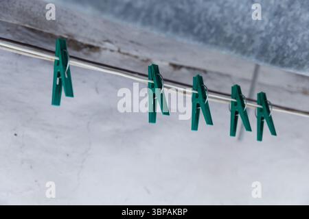 Eine Nahaufnahme farbenfroher grüner Kleiderschalen, die an einem Metalldraht vor einem weich strukturierten Hintergrund in einer häuslichen Umgebung hängen Stockfoto