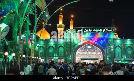 Besucher mit unterschiedlichem Hintergrund treffen sich friedlich am hell beleuchteten Imam Hussein-Schrein in Karbala zu einem religiösen Ereignis. Stockfoto