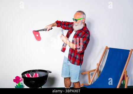 Älterer Mann grillt in einem legeren Outfit mit einer entspannten Umgebung und lebhaftem Tageshintergrund, Sommergrillszene Stockfoto