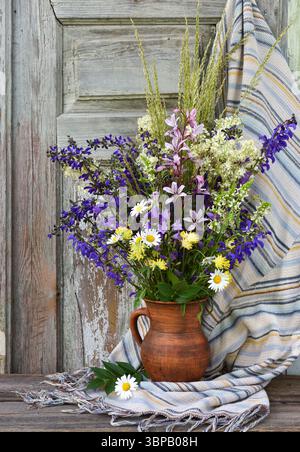 Stillleben mit Blumenstrauß in einem Tonkrug auf einem alten hölzernen Hintergrund. Blumenstrauß mit bunten Wildblumen Stockfoto