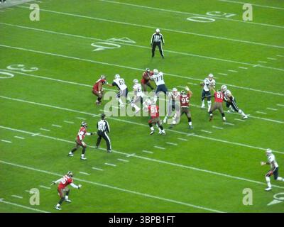 American Football-Spiel in Aktion zwischen zwei Teams auf einem grasbewachsenen Stadionfeld, mit Spielern in rot-weißen Uniformen und Schiedsrichtern Stockfoto