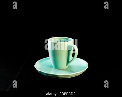 Minimalistisches Foto einer mintgrünen Kaffeetasse auf einer passenden Untertasse, platziert auf einem schwarzen Stoffhintergrund Stockfoto