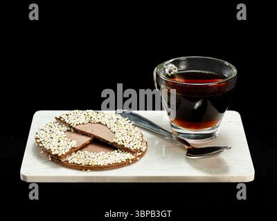 Eine Glasschale heißer Kaffee kombiniert mit einer traditionellen mexikanischen Schokolade und einem gepufften Amaranth-Keks auf einer weißen Marmorplatte mit einem Löffel Stockfoto