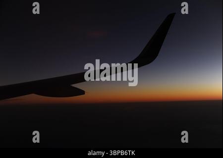 Flugzeugflügel während des Fluges in der Luft über den Wolken bei Dämmerung und Sonnenaufgang mit klarem Himmel mit klarer Horizontlinie im Sommer Stockfoto