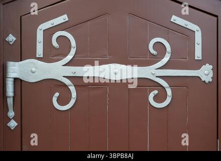 Dekoratives Scharnier mit feiner Ornamentik an dunkler Holztür. Historischer Charme, handgefertigte Details. Kopierraum. Stockfoto
