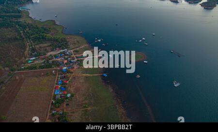 Ein atemberaubender Blick aus der Luft fängt das sanfte Leuchten des Sonnenaufgangs ein, das goldene Reflexe über das ruhige Wasser des Vajiralongkorn-Staudamms wirft. Gepunktet mit lu Stockfoto