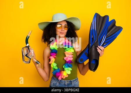 Fröhliche junge Frau mit Schnorchelausrüstung und farbenfrohem lei vor hellgelber Kulisse, die Reisen und Abenteuer repräsentiert Stockfoto