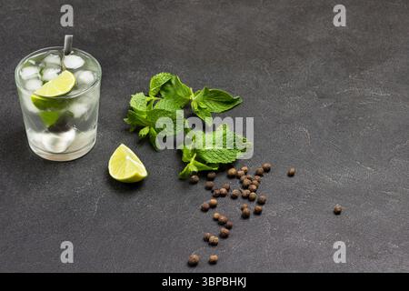 Ein Glas erfrischendes Getränk mit Limette, Minze und Eis. Limettenscheiben und Minzblätter auf dem Tisch. Kopierbereich. Schwarzer Hintergrund. Draufsicht Stockfoto