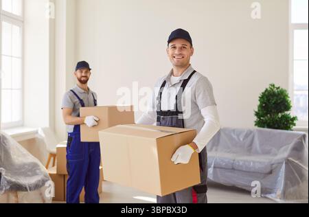 Lächelnde Profis in einheitlich tragenden Kartonschachteln, die beim Umsiedeln helfen. Stockfoto