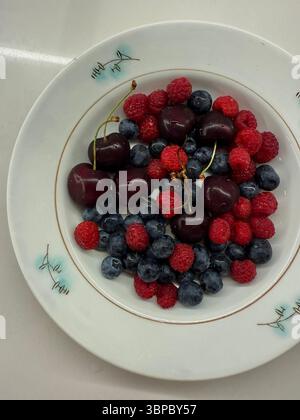 Diese Abbildung zeigt eine Ansicht von oben nach unten einer weißen Keramikplatte mit Kirschen, Heidelbeeren und Himbeeren. Die Früchte werden auf natürliche Weise auf die Platte gelegt Stockfoto