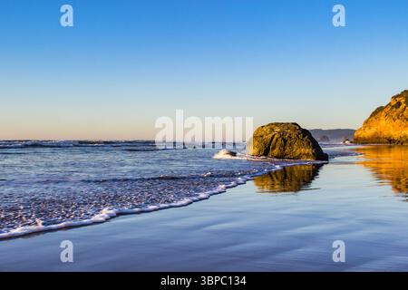 Hug Point State Park, Oregon – 28. November 2015: Wellen umrunden sanft das Ufer und reflektieren das goldene Licht der untergehenden Sonne auf dem nassen Sand. Stockfoto