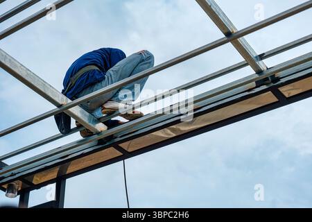 Bauarbeiter, der im Freien auf der Baustelle an einem Stahlrahmen der Dachkonstruktion montiert und geschweißt hat Stockfoto