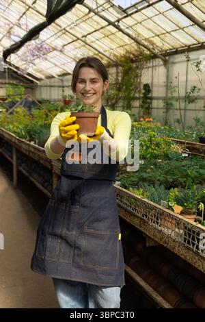 Die junge Frau präsentiert eine frisch vergossene Pflanze mit Sorgfalt und Präzision. Stockfoto