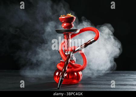 Shisha auf Holztisch mit Rauch vor schwarzem Hintergrund Stockfoto