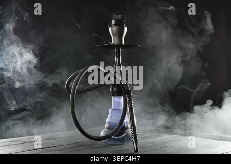 Shisha auf Holztisch mit Rauch vor schwarzem Hintergrund Stockfoto