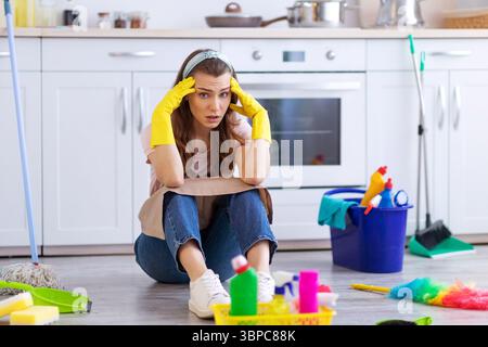 Ich brauche Pause. Erschöpfte Hausfrau oder Dienstmädchen sitzen auf dem Boden in der Küche zwischen Reinigungsmitteln, halten den Kopf in Angst Stockfoto