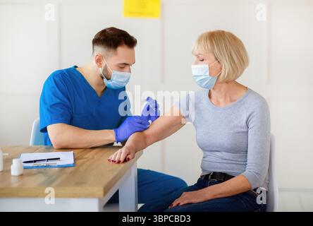 Ältere Dame, die in der Klinik gegen Coronavirus geimpft wird und an einer antiviralen Kampagne teilnimmt Stockfoto