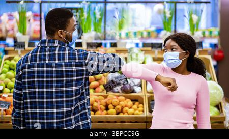 Millennial schwarze Frau und Mann in Gesichtsmasken Gruß jeder Andere durch Berühren Ellbogen im Supermarkt während covid-19 Stockfoto