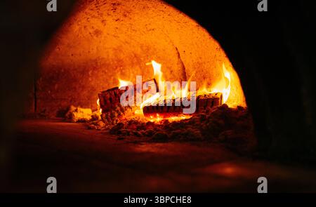 Ein Holzfeuer in einem Backofen. Das Feuer ist orange und gelb. Der Ofen ist offen und das Feuer ist drinnen Stockfoto