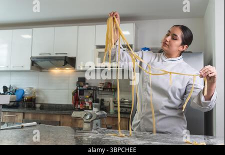 Der professionelle Koch hält frische hausgemachte Pasta, nachdem er sie mit einer Nudelmaschine zubereitet hat Stockfoto