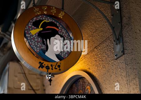 Rundes Händlerschild mit Ukiyo-e-Kunst hängt vor dem Tateyama-Geschäft entlang der Yanaka Ginza-Straße in der Altstadt von Yanesen, Tokio, Japan. Stockfoto