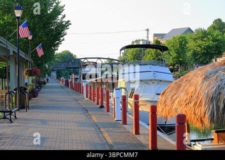 Fairport, NY, USA - 2. Juli 2025 - Frau geht auf dem roten Backsteinkanal durch das Dorf Fairport. Die Boote sind am Kanal festgebunden, wi Stockfoto