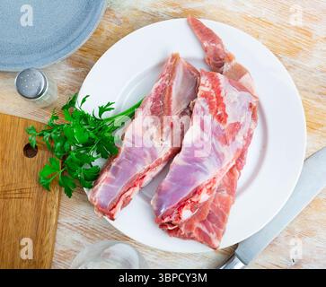 Frische Schweinerippchen auf weißer Keramikplatte mit Petersilie auf dem Tisch Stockfoto
