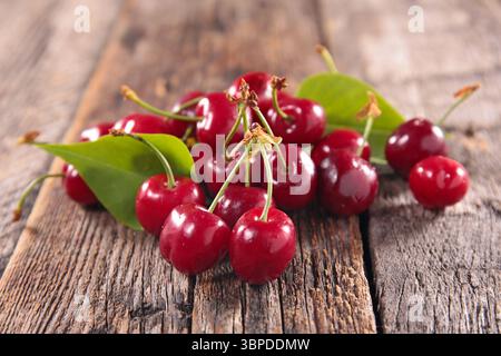 Eine Nahaufnahme einer Gruppe frischer, reifer roter Kirschen mit grünen Blättern, kunstvoll auf einem rustikalen Holzhintergrund angeordnet. Ideal für Food Blogs, Rec Stockfoto