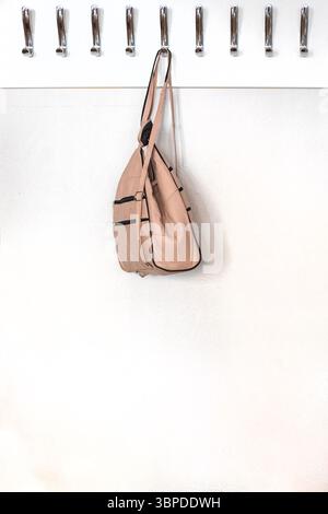 Heller Lederrucksack, der an einem Kleiderbügel mit Metallhaken hängt, in einem Klassenzimmer, Büro. Zurück zur Schule Stockfoto