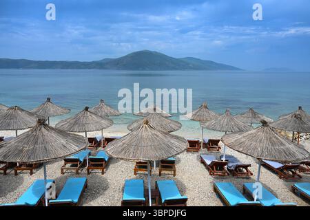 Sonnenschirme und Liegen am Strand in Albanien. Wunderschöner Blick vom Strand auf das Meer und die Berge Stockfoto