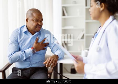 Männlicher Patient, der seine Brust schmerzhaft hält, während er mit einer Ärztin spricht Stockfoto