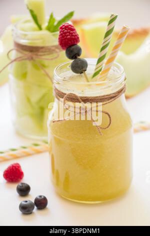 Zwei stilvolle Gläser mit fruchtigen Getränken stehen auf einem Tisch, geschmückt mit frischen Himbeeren, Heidelbeeren und Minze. Perfekt für Outdoor-Vergnügen. Stockfoto