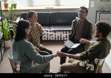 Verschiedene junge Erwachsene, die an Gruppentherapiesitzungen teilnehmen und Hände halten Stockfoto