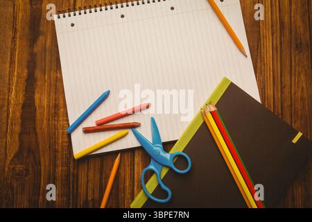 Das flache Design zeigt ein offenes spiralförmiges Notizbuch auf einem Holztisch mit Buntstiften, Bleistiften und Scheren Stockfoto