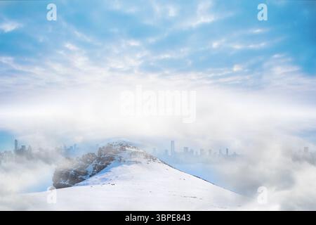 Der schneebedeckte Kamm erhebt sich in flachem Design über niedrigen Wolken und offenbart die Skyline der Stadt Stockfoto