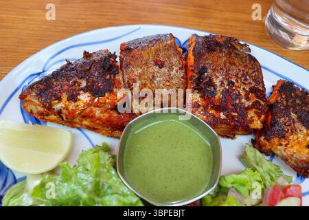 Perfekt gegrillter Tandoori-Forellenfisch, serviert mit würzigem grünem Chutney, Zitronenkeil und frischem grünem Salat. Ein schmackhaftes indisches Gericht. Stockfoto