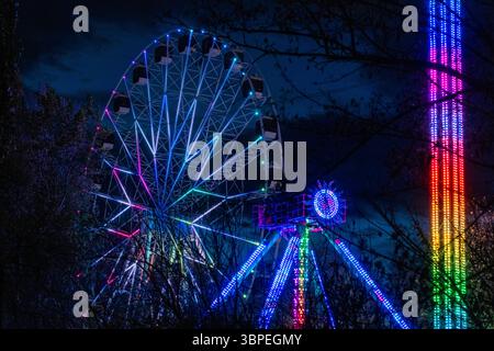 Im Victory Park, Jerewan, Armenien, gibt es ein Riesenrad und eine nahe gelegene Vergnügungsfahrt, die mit leuchtenden bunten Lichtern vor dem Nachthimmel beleuchtet ist Stockfoto