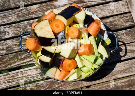 Lebendige Auswahl an frisch gehacktem Gemüse, einschließlich Karotten, Zucchini und Auberginen, in einer Schüssel auf einem rustikalen Holztisch im Freien Stockfoto