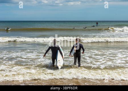 East Cliff Beach, Bournemouth, Großbritannien - 28. Mai 2025: Zwei Surfer gehen mit Surfbrettern ins Meer. Stockfoto