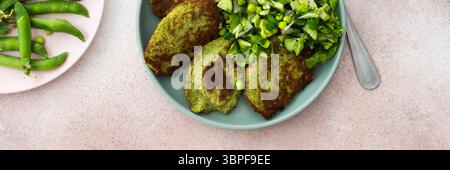 Genießen Sie Zucchini- und Brokkoli-Pfannkuchen kombiniert mit einem frisch gemischten Salat mit Gurken, jungen Erbsen und Radieschen. Ein köstlicher und gesunder Vegetarier Stockfoto
