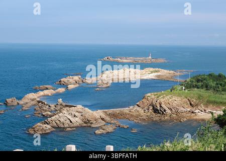Atemberaubender Blick auf die Küste mit felsigen Felsvorsprüngen und einem Leuchtturm vor einem klaren blauen Himmel und einer ruhigen Meereslandschaft Stockfoto