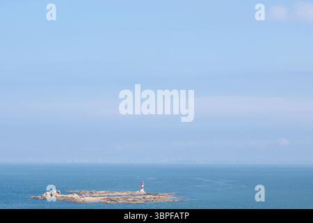 Eine ruhige Küstenlandschaft mit einem beeindruckenden Leuchtturm auf einer Felseninsel, umgeben von ausgedehntem Meereswasser und einem klaren blauen Himmel Stockfoto