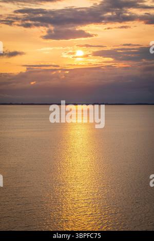 Atemberaubender Sonnenuntergang über dem Meer in der Nähe von Dänemark, von einem Kreuzfahrtschiff erfasst. Windturbinen bilden den Horizont unter leuchtendem Rot- und Orangenhimmel. Stockfoto