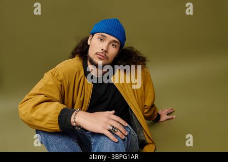 Stilvoller junger bärtiger Mann entspannt sich auf dem Studioboden in trendigen Klamotten. Stockfoto
